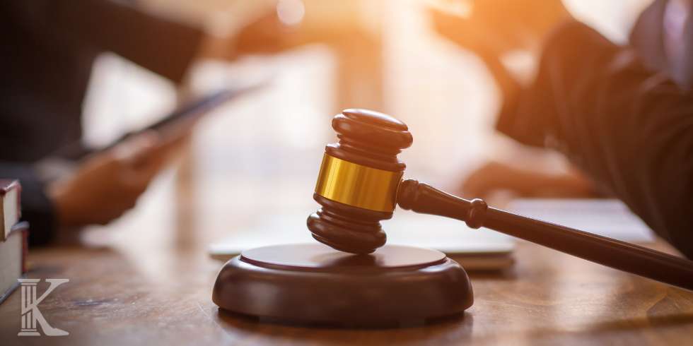 Młotek sędziowski, kancelaria prawna, rozmowa dwóch osób w tle