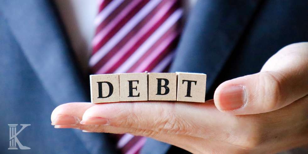 Dłoń trzymająca drewniane klocki z napisem "DEBT" - dług