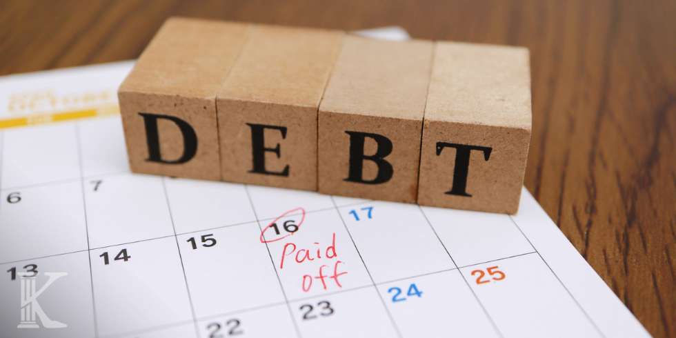 Drewniane klocki z napisem "DEBT" - dług, leżące na kartce z kalendarza