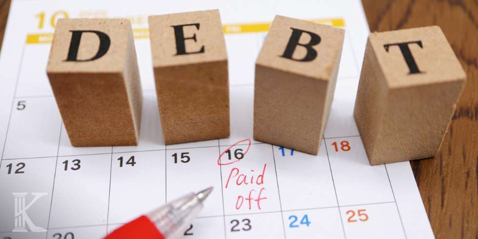 Drewniane klocki z napisem "DEBT" - dług, leżące na kartce z kalendarza