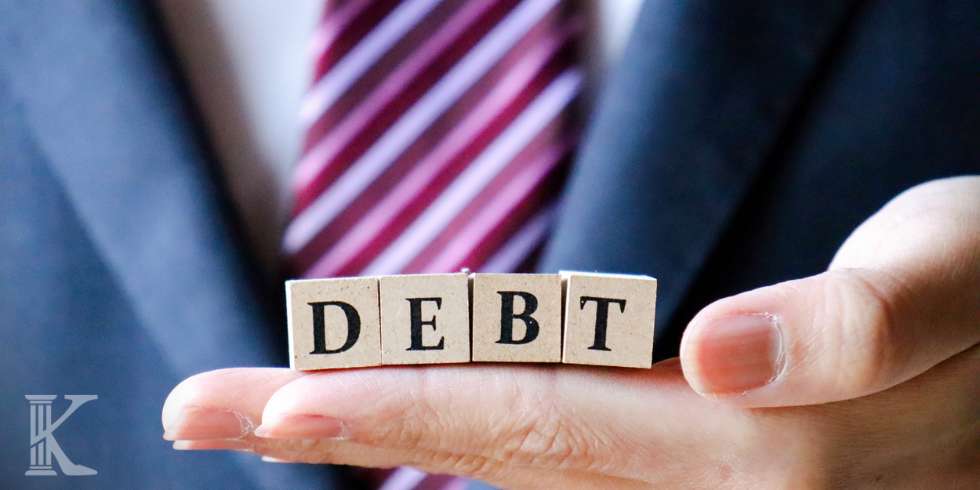 Osoba trzymająca klocki z napisem DEBT - DŁUG