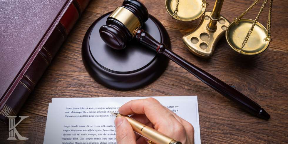 Hand writing on a legal document with a gavel and scales of justice on a wooden desk.