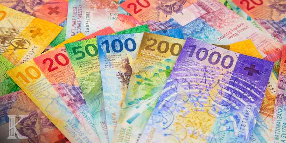 Kolorowy wachlarz banknotów franka szwajcarskiego o nominałach 10, 20, 50, 100, 200 i 1000 rozłożony na tle innych rozrzuconych pieniędzy CHF.