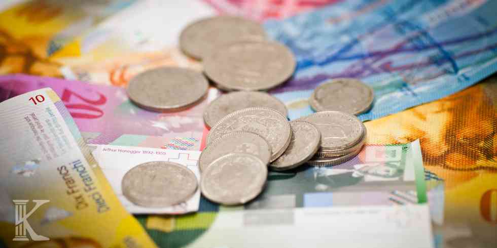 Srebrne monety franka szwajcarskiego rozrzucone na kolorowych banknotach CHF o różnych nominałach.