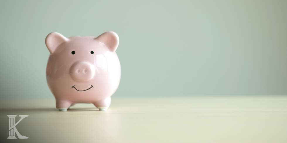 Pink piggy bank with a smile sits on a pale surface against a soft pastel green background, suggesting savings.