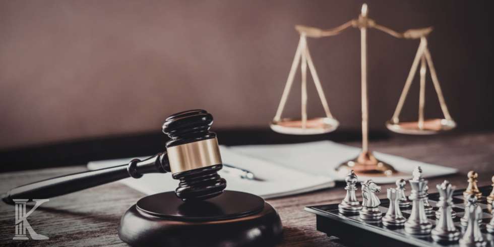 Gavel on a wooden table with scales of justice and chess pieces in the background, symbolizing law and strategy.