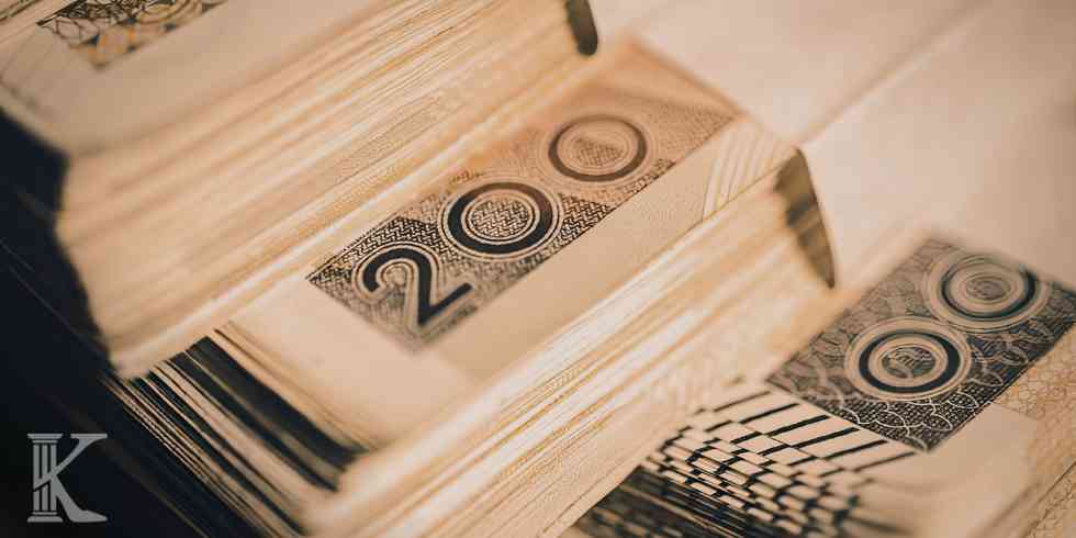 Młotek sędziowski na podstawce na biurku z dokumentami; w tle rozmyta postać prawnika.