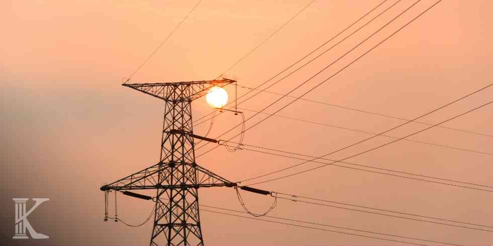 Lattice electricity pylon silhouetted against an orange sunset with power lines sprawling across the sky