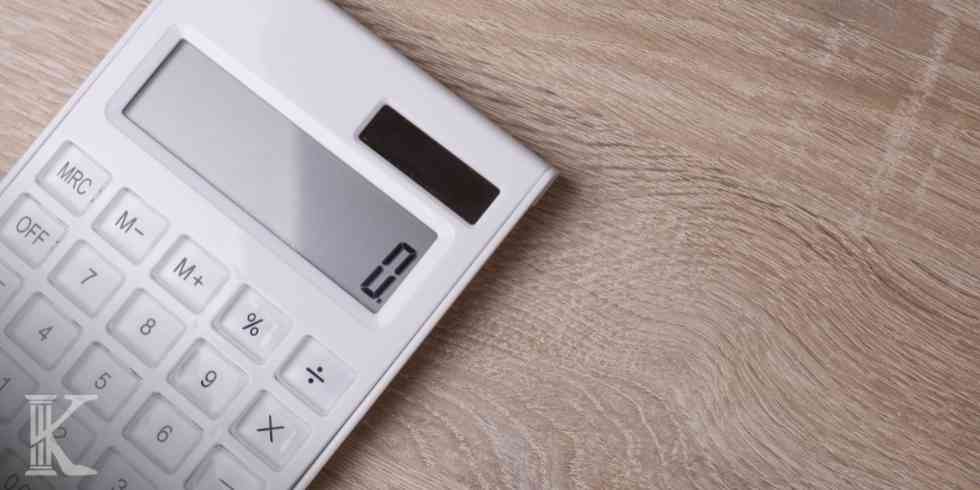 Biały kalkulator na drewnianym blacie służący do analizy sytuacji finansowej i zadłużenia.