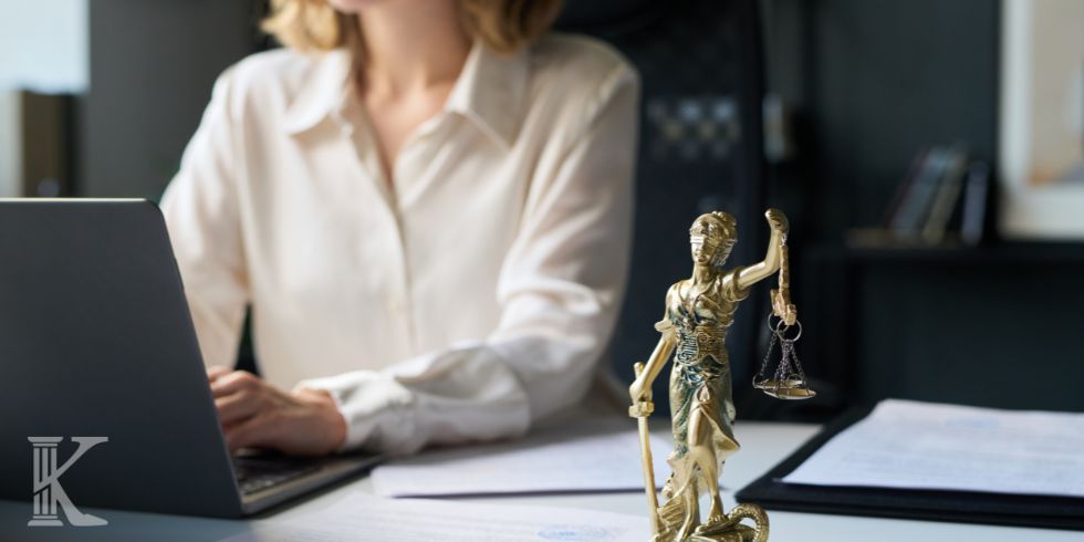 Statuetka Temidy stoi na biurku prawnika analizującego dokumenty na laptopie.
