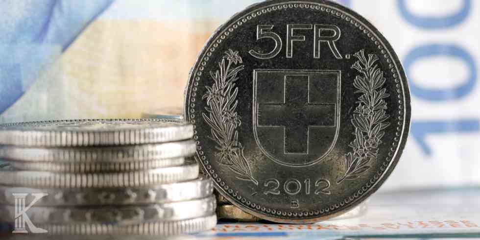 Srebrna moneta 5 franków szwajcarskich na tle banknotów – ilustracja do tematu rozliczeń kredytów.