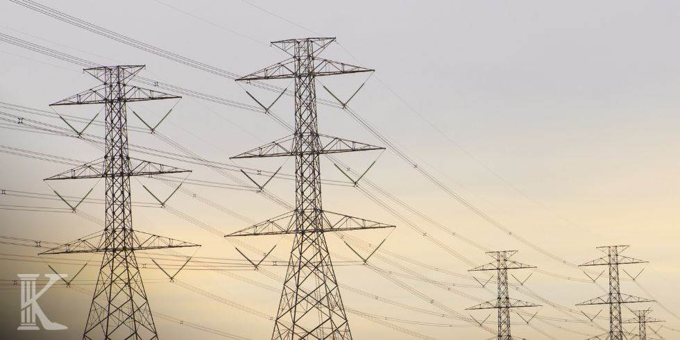 Electrical transmission towers with high-voltage lines against a pale sunset sky.