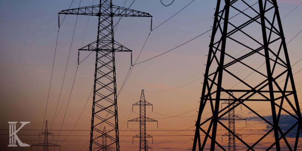 High-voltage power lines and lattice towers silhouetted against a sunset sky.