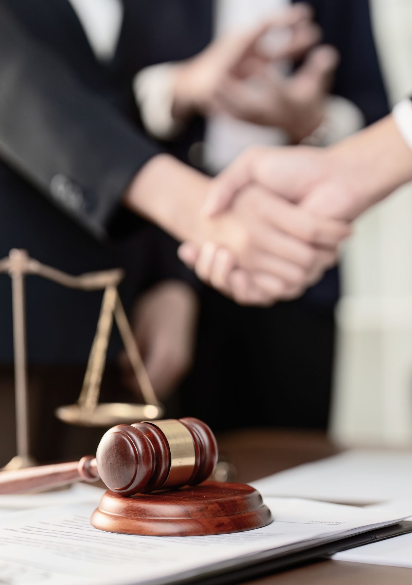 Wooden gavel rests on legal documents with blurred hands in the background, conveying justice. (Informative)
